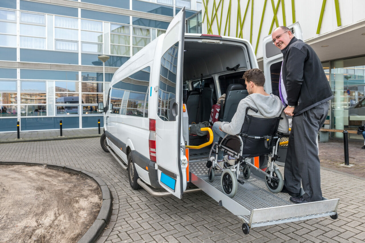 Ein Mann hilft einer Person im Rollstuhl in einen Transporter, der mit moderner Fahrzeugortung ausgestattet ist.
