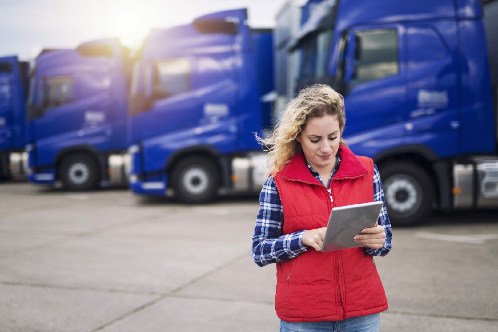 Eine Frau in roter Weste nutzt ein Tablet zur GPS Ortung vor einer Reihe blauer Lastwagen.